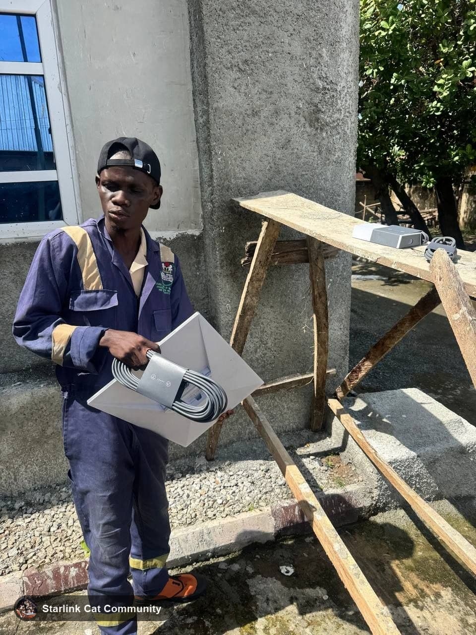 The installer holding the Starlink dish and cable in front of the hospital building
